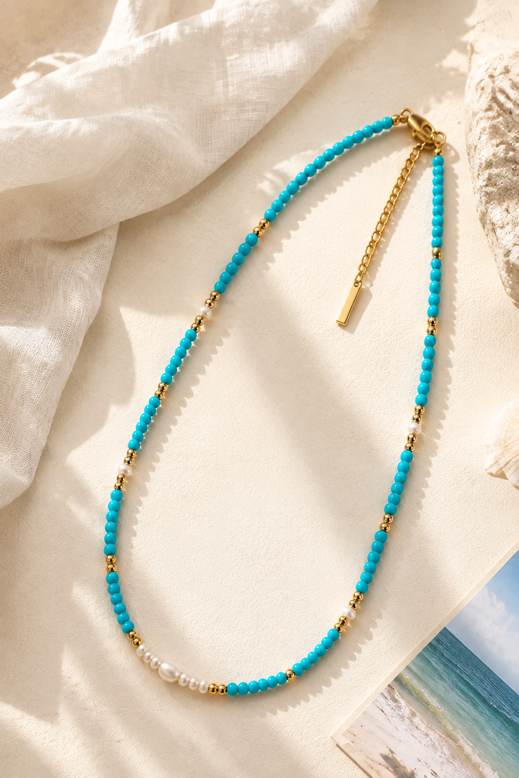 Coastal-inspired beaded necklace strand featuring 3mm turquoise stones and freshwater pearls, resting gracefully on a warm aesthetic stone surface.