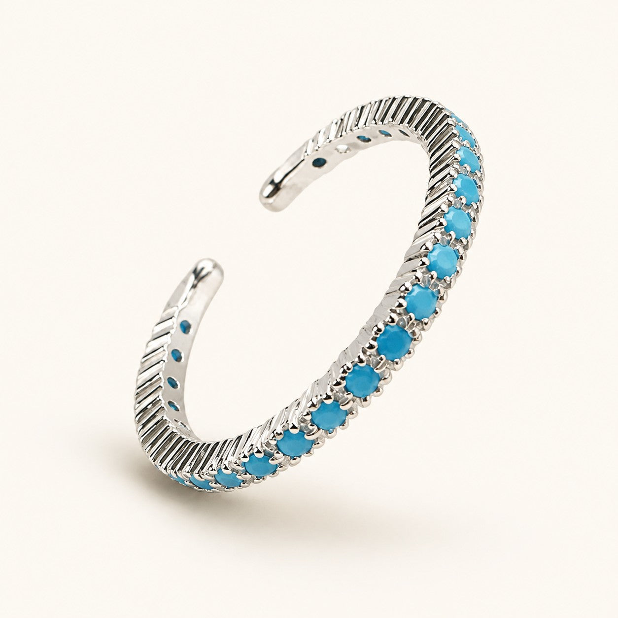 Silver plated adjustable open ring set with a row of vibrant turquoise blue stones on cream background
