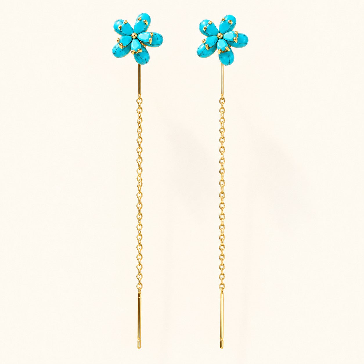Pair of gold threader drop earrings featuring turquoise blue flower studs on isolated cream background