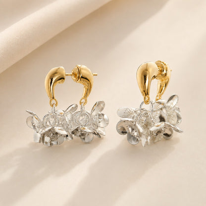 Pair of two-tone gold arch and silver petal floral cluster drop earrings on beige fabric