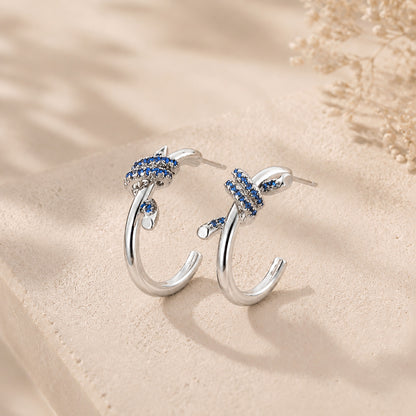 Vintage white gold-tone knotted C-hoop earrings with sapphire blue details displayed elegantly on warm stone and soft silk.