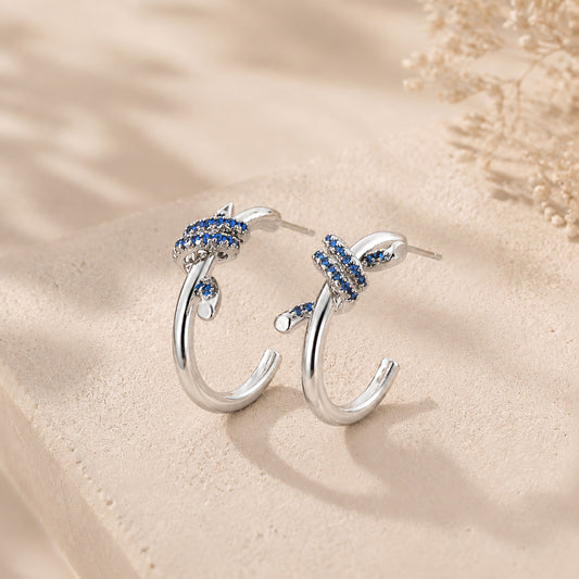 Vintage white gold-tone knotted C-hoop earrings with sapphire blue details displayed elegantly on warm stone and soft silk.