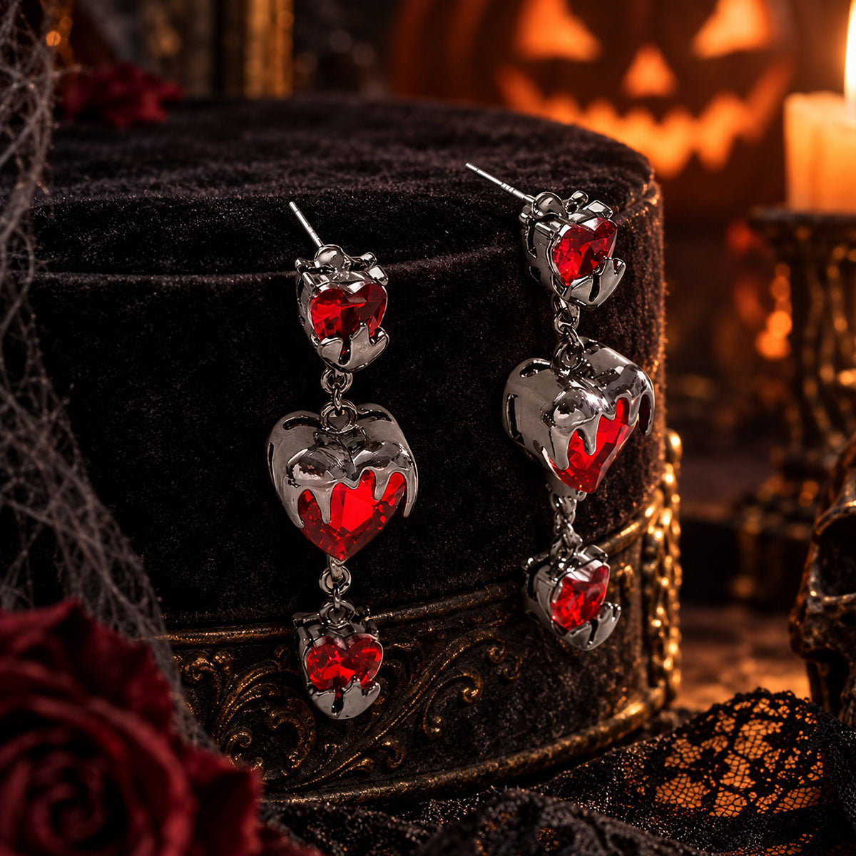 Gothic red heart crystal drop earrings on black velvet stand surrounded by candles and Halloween pumpkin