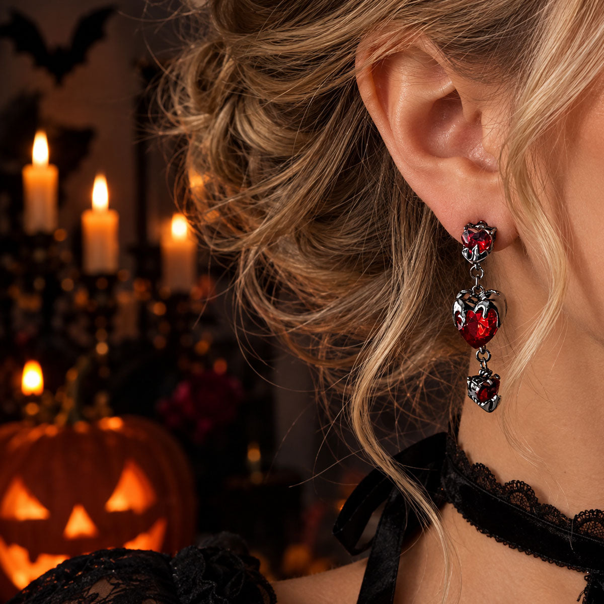 Side profile of model wearing vampire-style red heart drop earrings with candlelit Halloween background