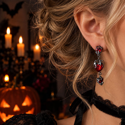 Side profile of model wearing vampire-style red heart drop earrings with candlelit Halloween background