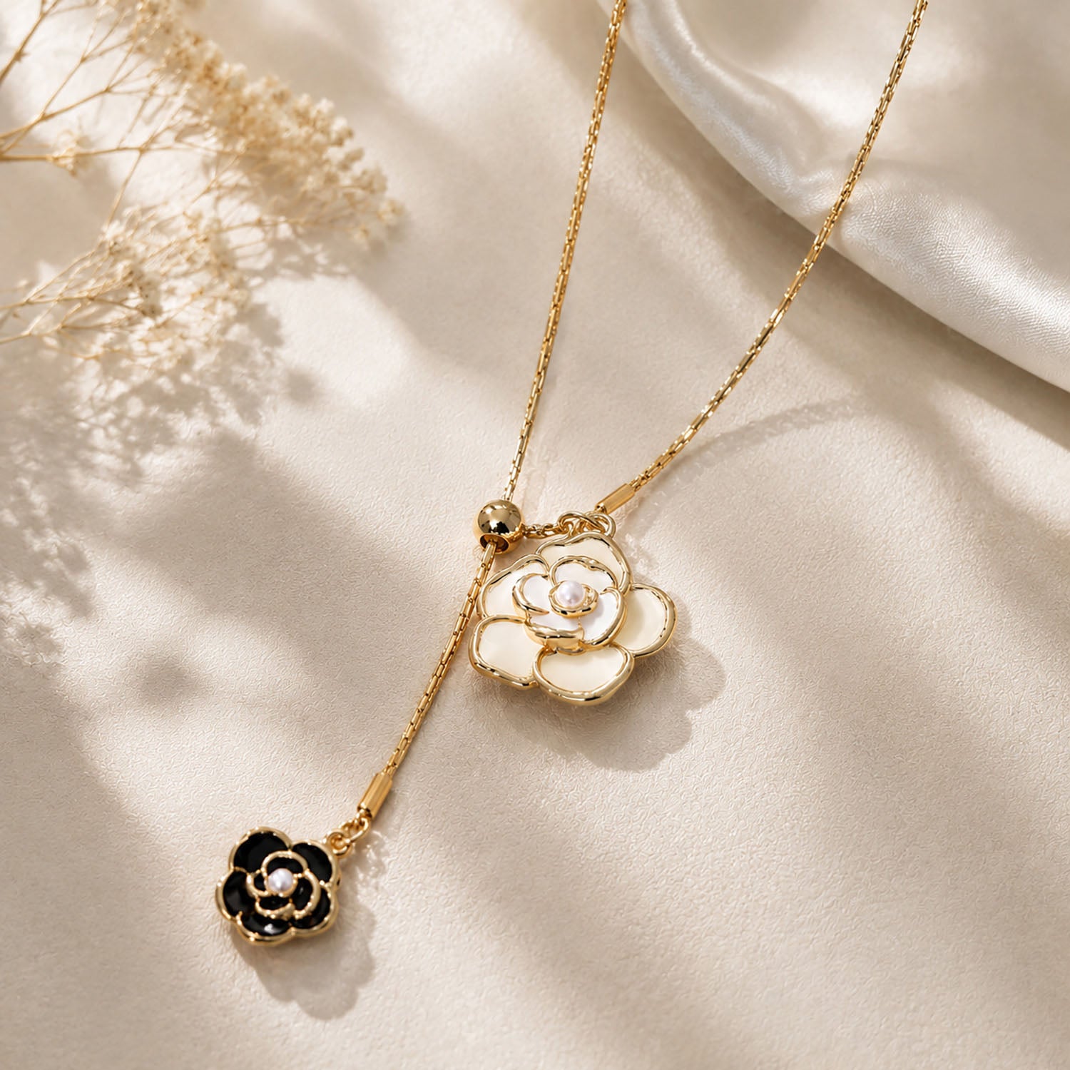 Close-up of an elegant gold-tone black and white camellia drop necklace resting on a textured aesthetic surface with soft silk.