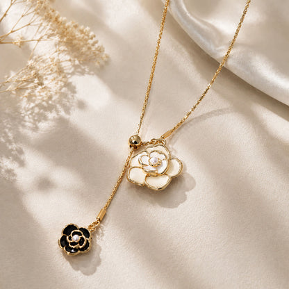 Close-up of an elegant gold-tone black and white camellia drop necklace resting on a textured aesthetic surface with soft silk.