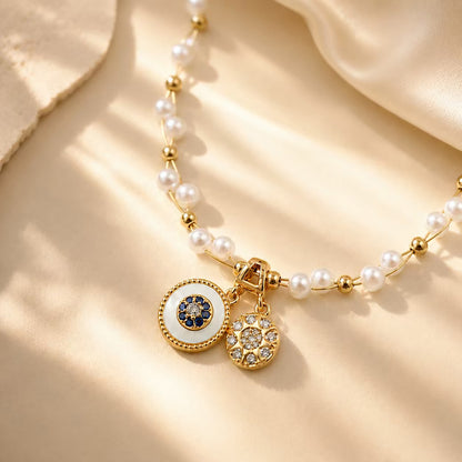 Close up of gold-tone double disc pendants with intricate details on a pearl beaded necklace.