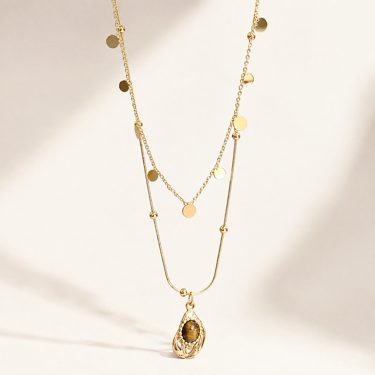 Flatlay view of double layered gold necklace with sequin chain and teardrop resin tiger's eye pendant