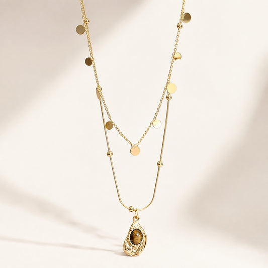 Flatlay view of double layered gold necklace with sequin chain and teardrop resin tiger's eye pendant