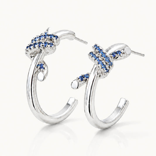 Detailed view of vintage white gold-tone C-hoop earrings featuring intricate blue zirconia knots on a white background.