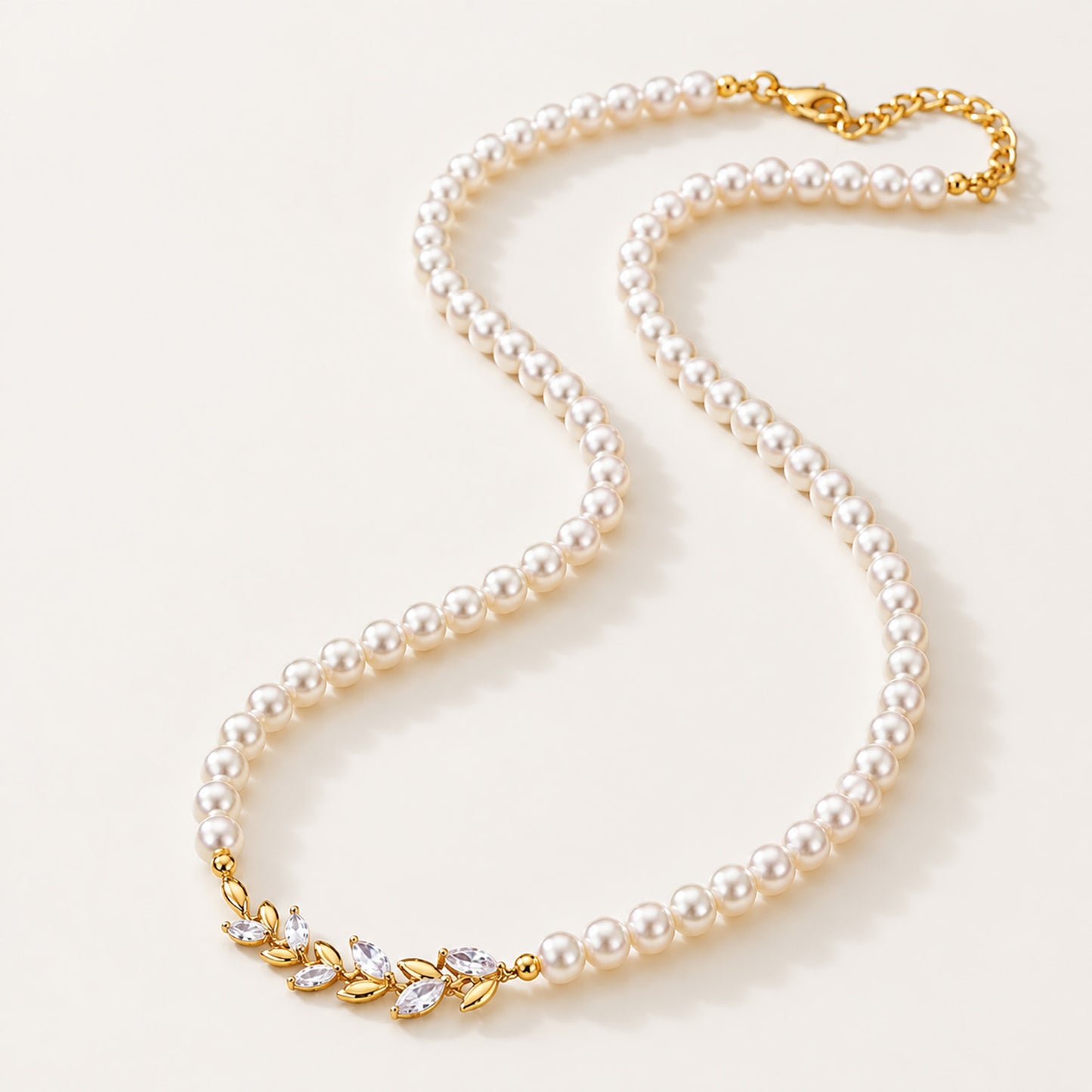 Minimalist flat lay of a full strand simulated pearl necklace featuring a micro-paved gold-tone wheat ear centerpiece on a white background.