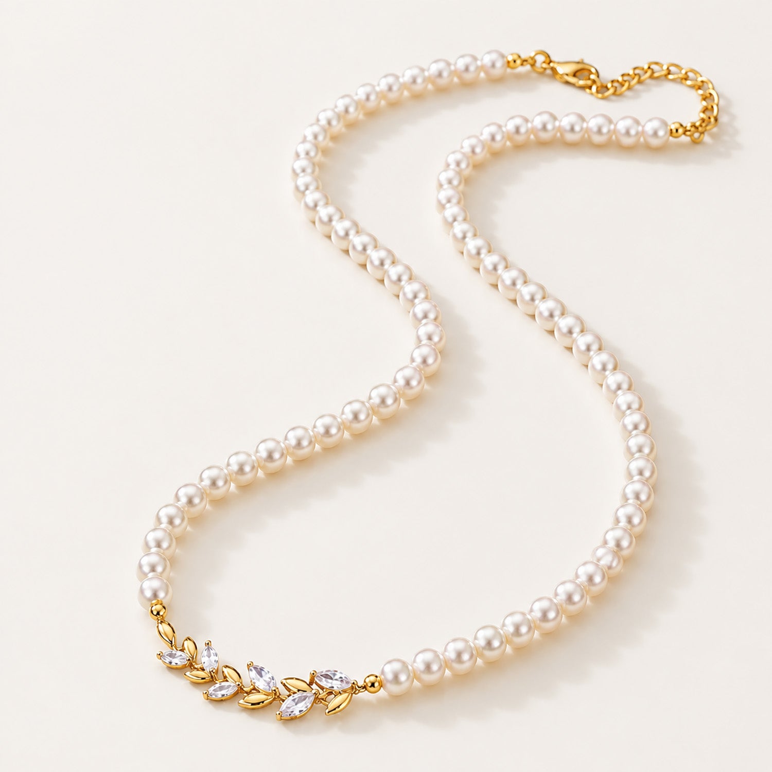 Minimalist flat lay of a full strand simulated pearl necklace featuring a micro-paved gold-tone wheat ear centerpiece on a white background.