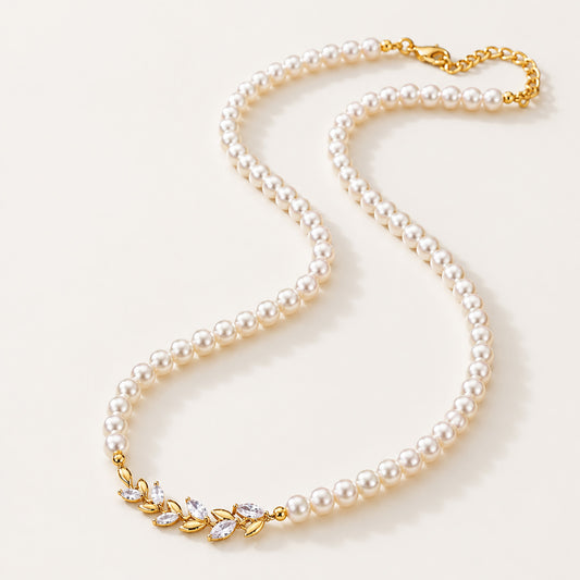 Minimalist flat lay of a full strand simulated pearl necklace featuring a micro-paved gold-tone wheat ear centerpiece on a white background.