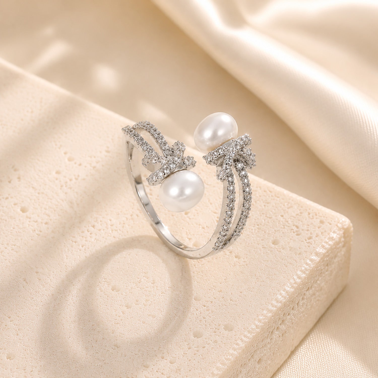 Elegant white gold-tone twisted rope ring with freshwater pearls resting gracefully on a textured block with soft silk.