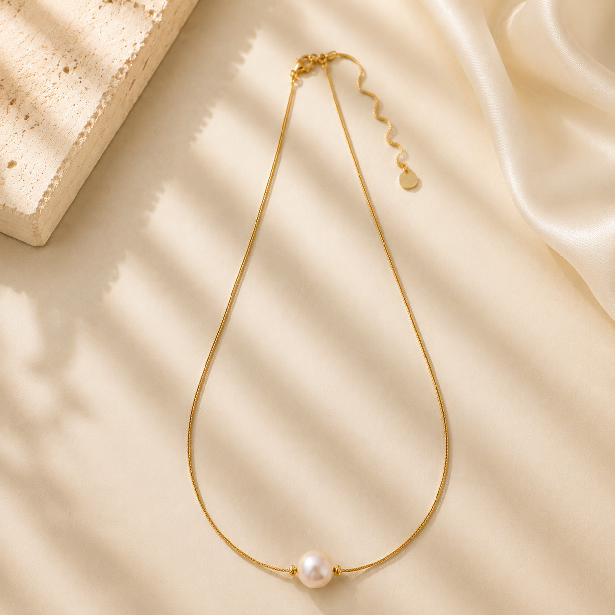 Close up of a vintage-inspired single aurora pearl pendant on a delicate gold-tone chain in soft light.