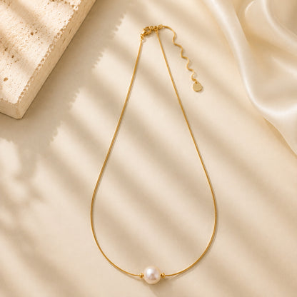 Close up of a vintage-inspired single aurora pearl pendant on a delicate gold-tone chain in soft light.