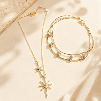 Elegant gold-tone layered necklace with cubic zirconia star and sunburst motifs displayed beautifully on an aesthetic stone and soft silk surface.