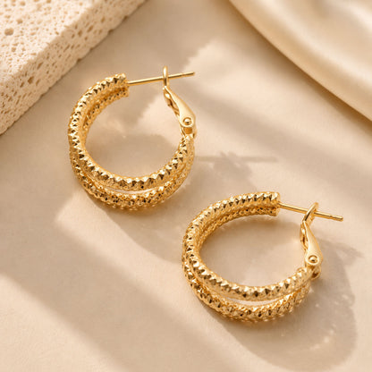 Close up of textured gold-tone hoop earrings resting on warm stone in soft sunlight.