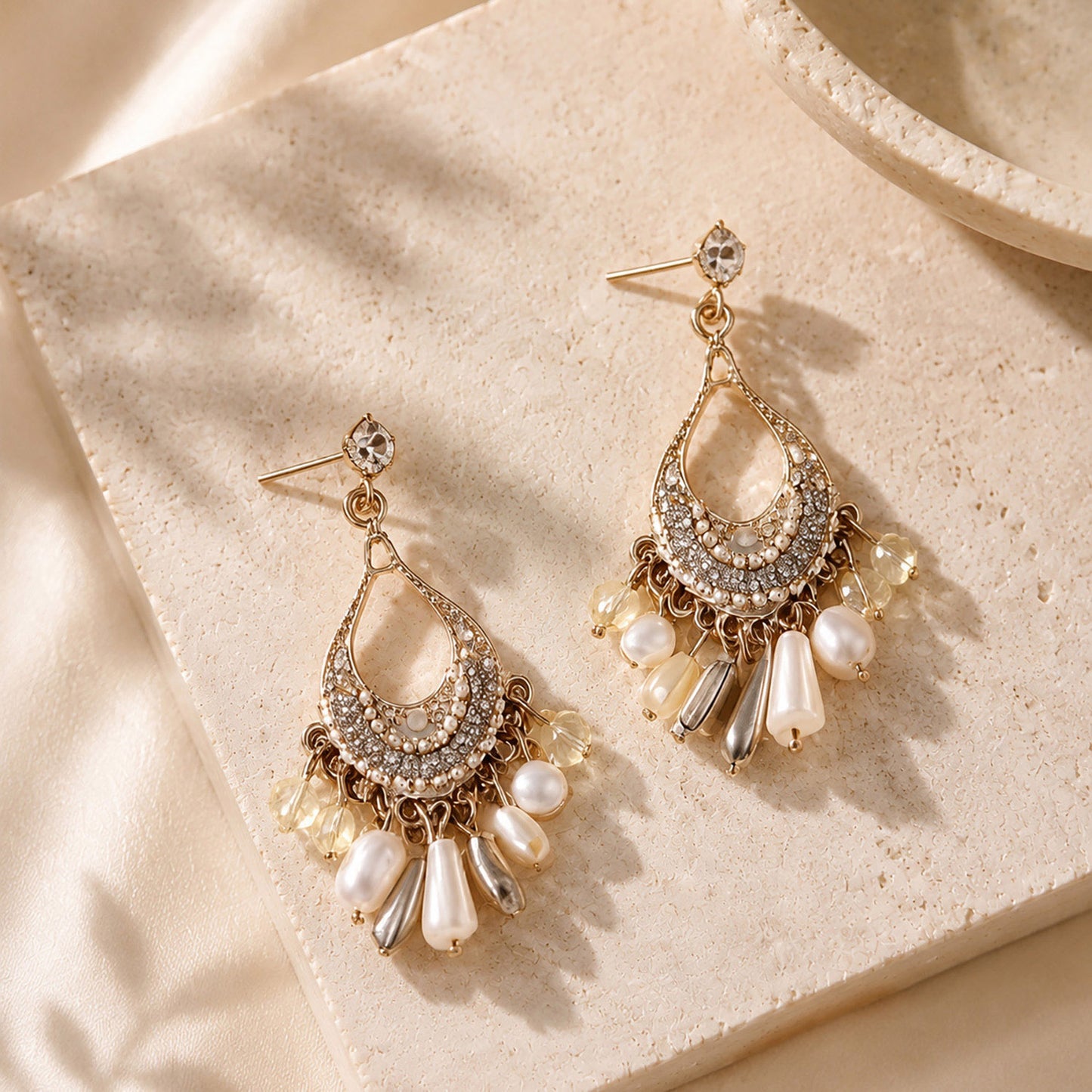Close up of intricate gold-tone bohemian chandelier earrings with white pearls and crystals resting on a warm stone surface.