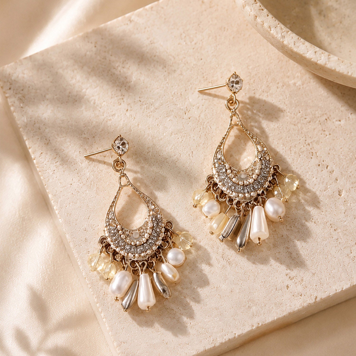 Close up of intricate gold-tone bohemian chandelier earrings with white pearls and crystals resting on a warm stone surface.