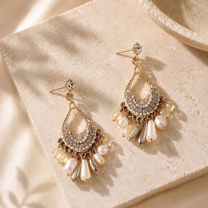 Close up of intricate gold-tone bohemian chandelier earrings with white pearls and crystals resting on a warm stone surface.