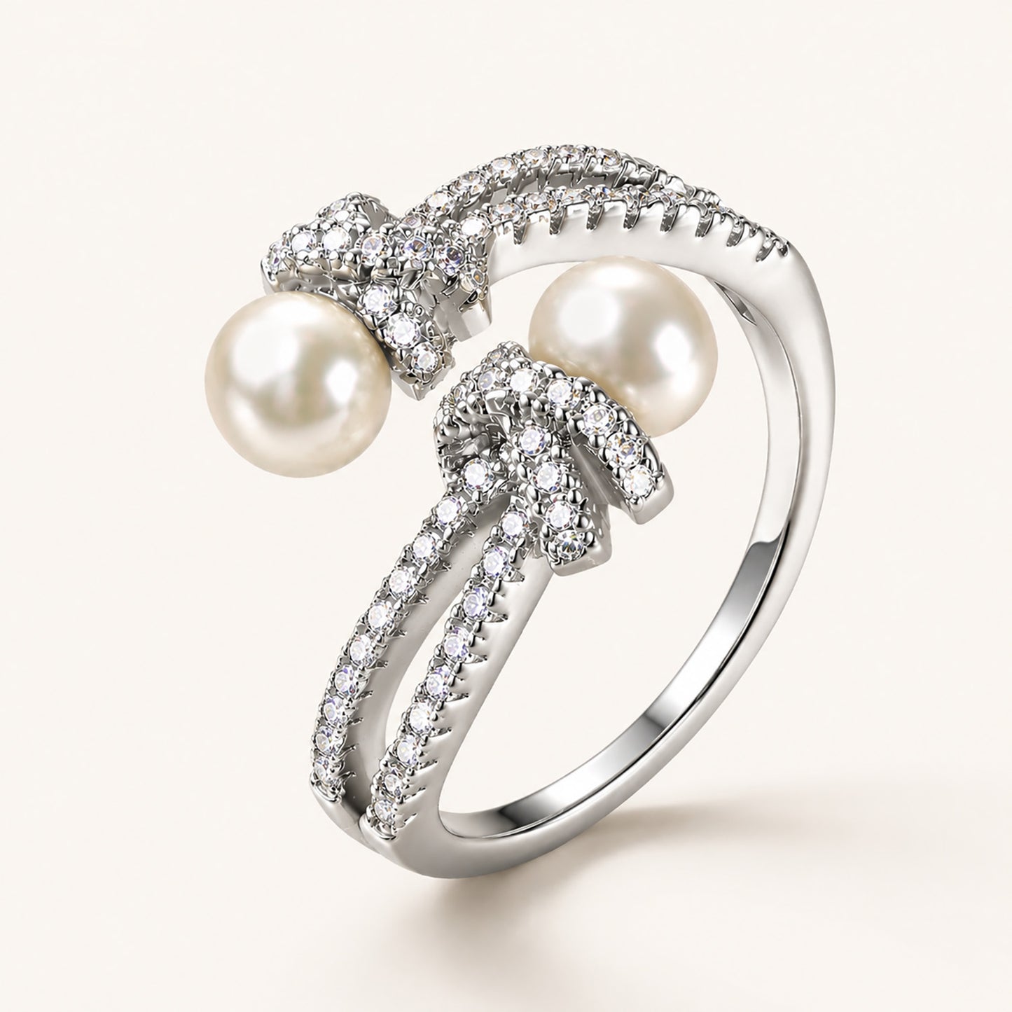 Detailed macro close-up of an 18K white gold-plated adjustable ring showing intricate micro-paved zircon knots and two freshwater pearls.