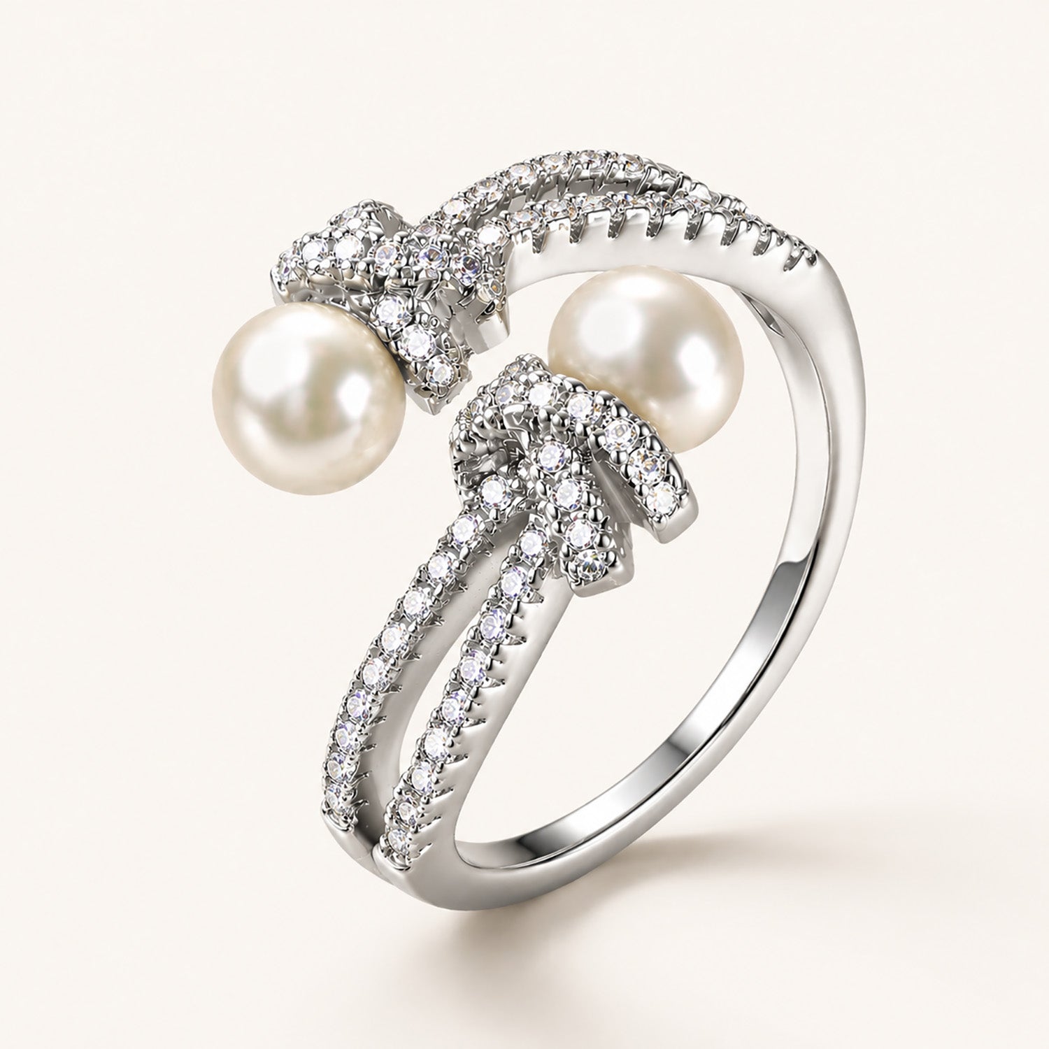 Detailed macro close-up of an 18K white gold-plated adjustable ring showing intricate micro-paved zircon knots and two freshwater pearls.