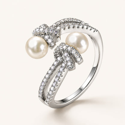 Detailed macro close-up of an 18K white gold-plated adjustable ring showing intricate micro-paved zircon knots and two freshwater pearls.