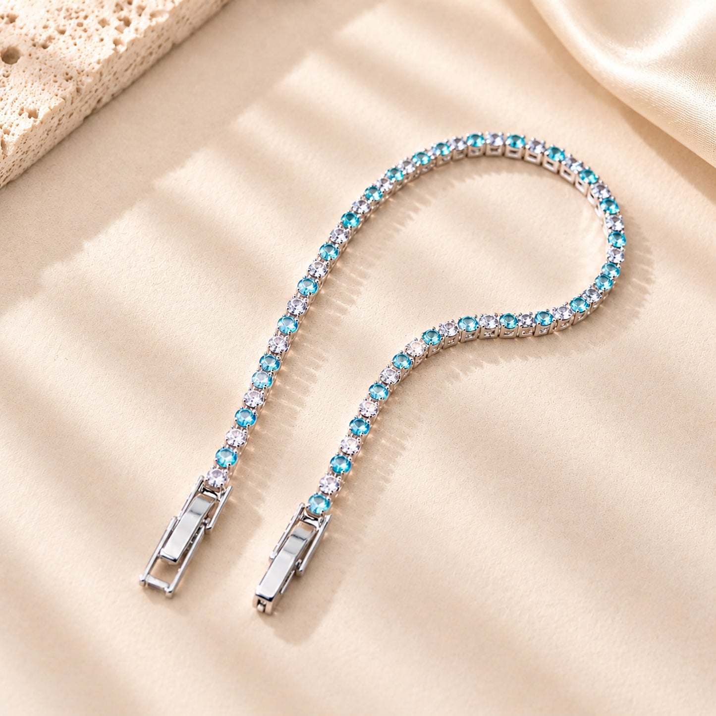 Macro detail of the secure clasp on a sparkling blue zirconia tennis bracelet resting on a textured plaster surface.