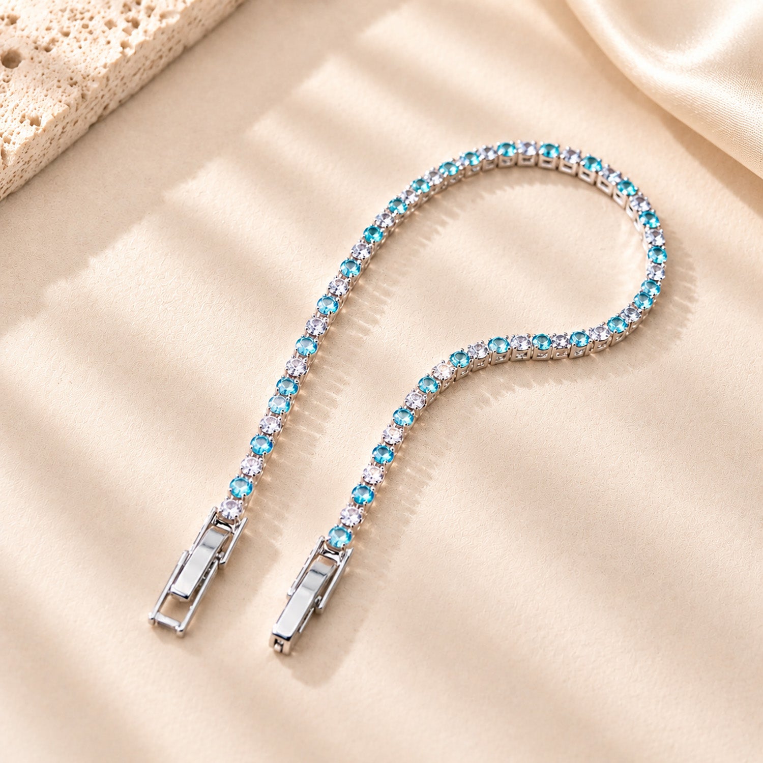 Macro detail of the secure clasp on a sparkling blue zirconia tennis bracelet resting on a textured plaster surface.
