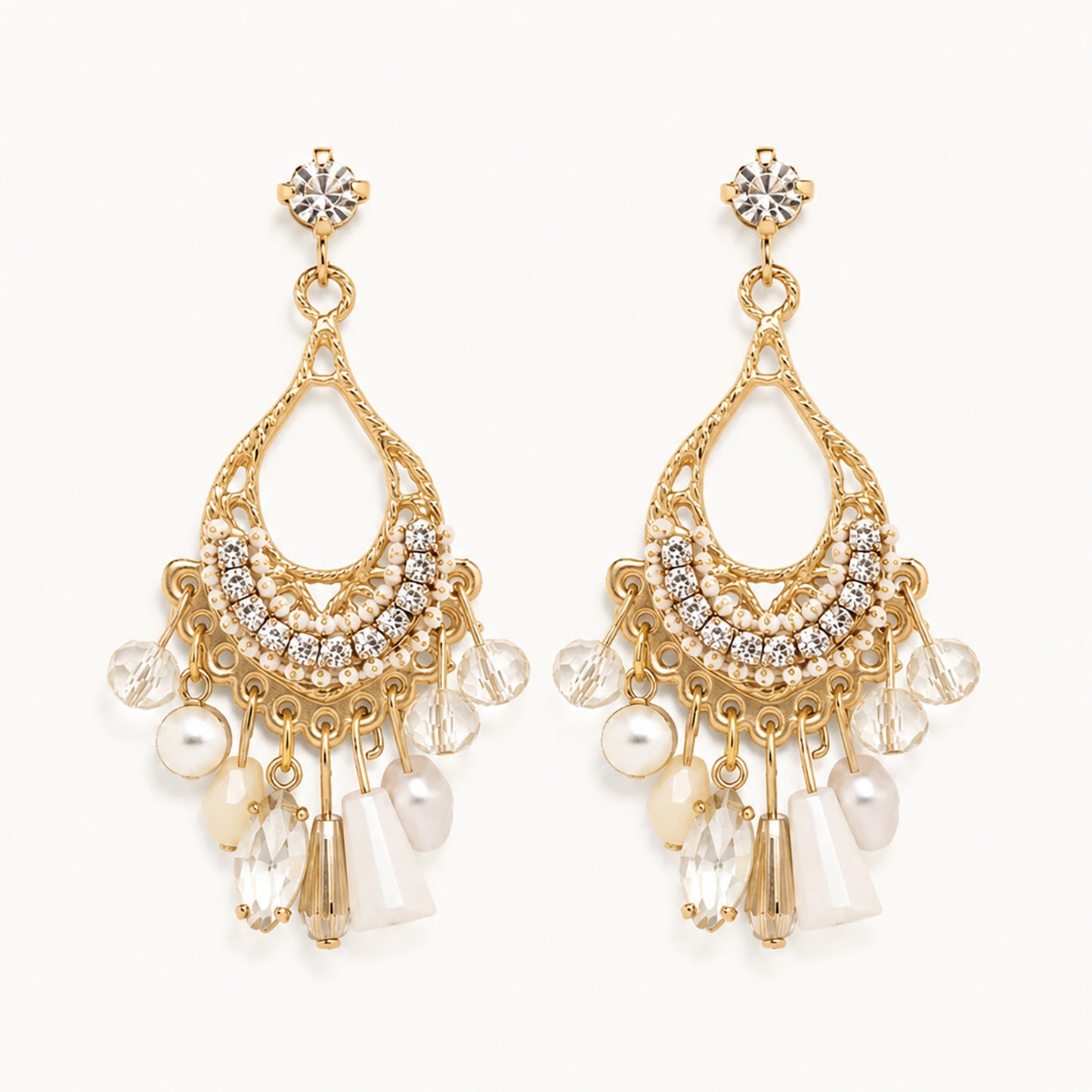 Detailed view of vintage-inspired gold-tone teardrop earrings with white crystal fringe and faux pearls on a white background.