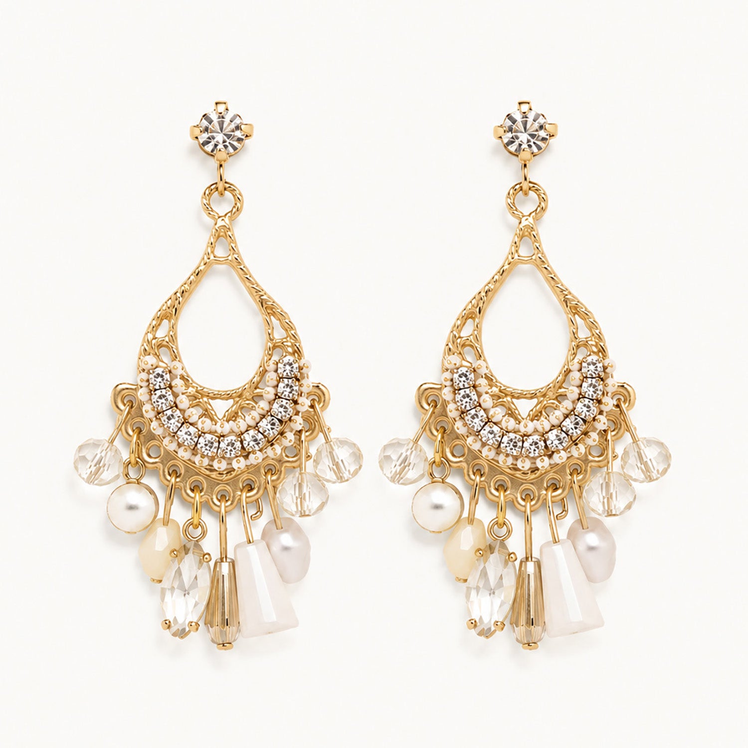 Detailed view of vintage-inspired gold-tone teardrop earrings with white crystal fringe and faux pearls on a white background.