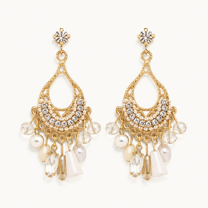 Detailed view of vintage-inspired gold-tone teardrop earrings with white crystal fringe and faux pearls on a white background.