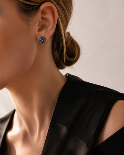Close-up of a woman's profile styling brilliant black halo stud earrings with a black outfit.