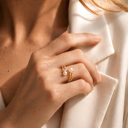 Elegant woman styling a gold-tone open ring featuring sparkling zircon knots and freshwater pearls against a white blazer.