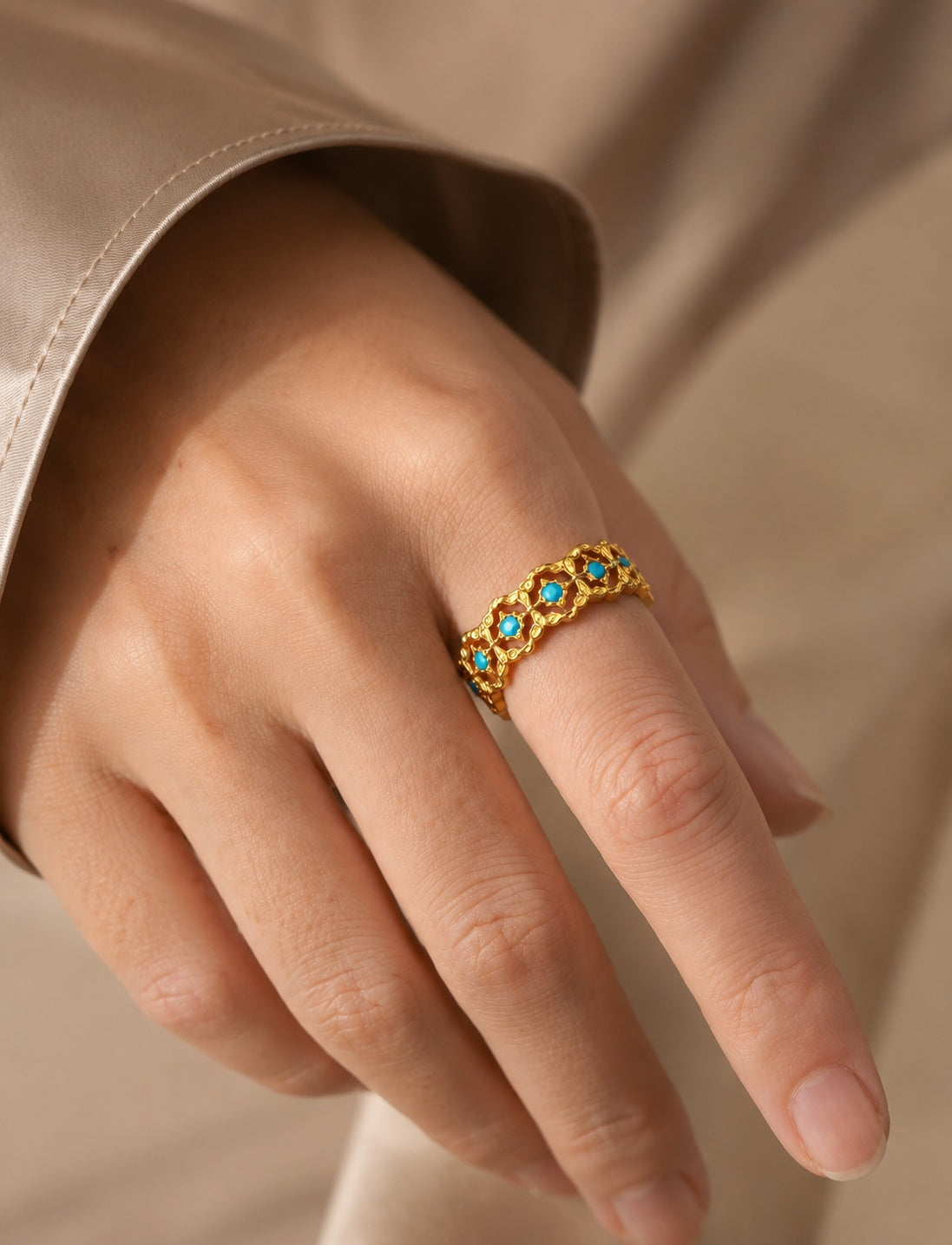 Close-up of a woman's hand wearing a stunning vintage-inspired turquoise and gold-tone cutout ring over a silk top.