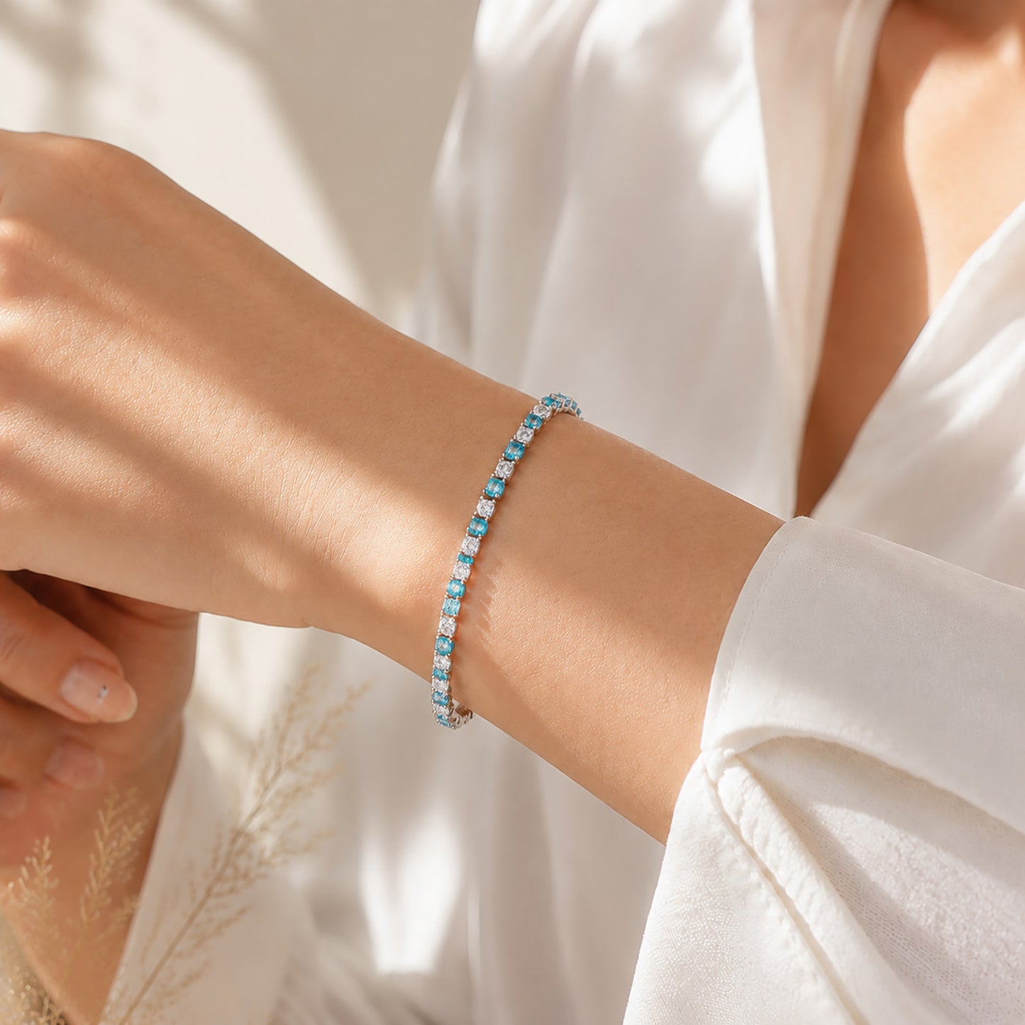 Close up of a woman wearing a sparkling blue zirconia tennis bracelet paired with a crisp white shirt in warm sunlight.