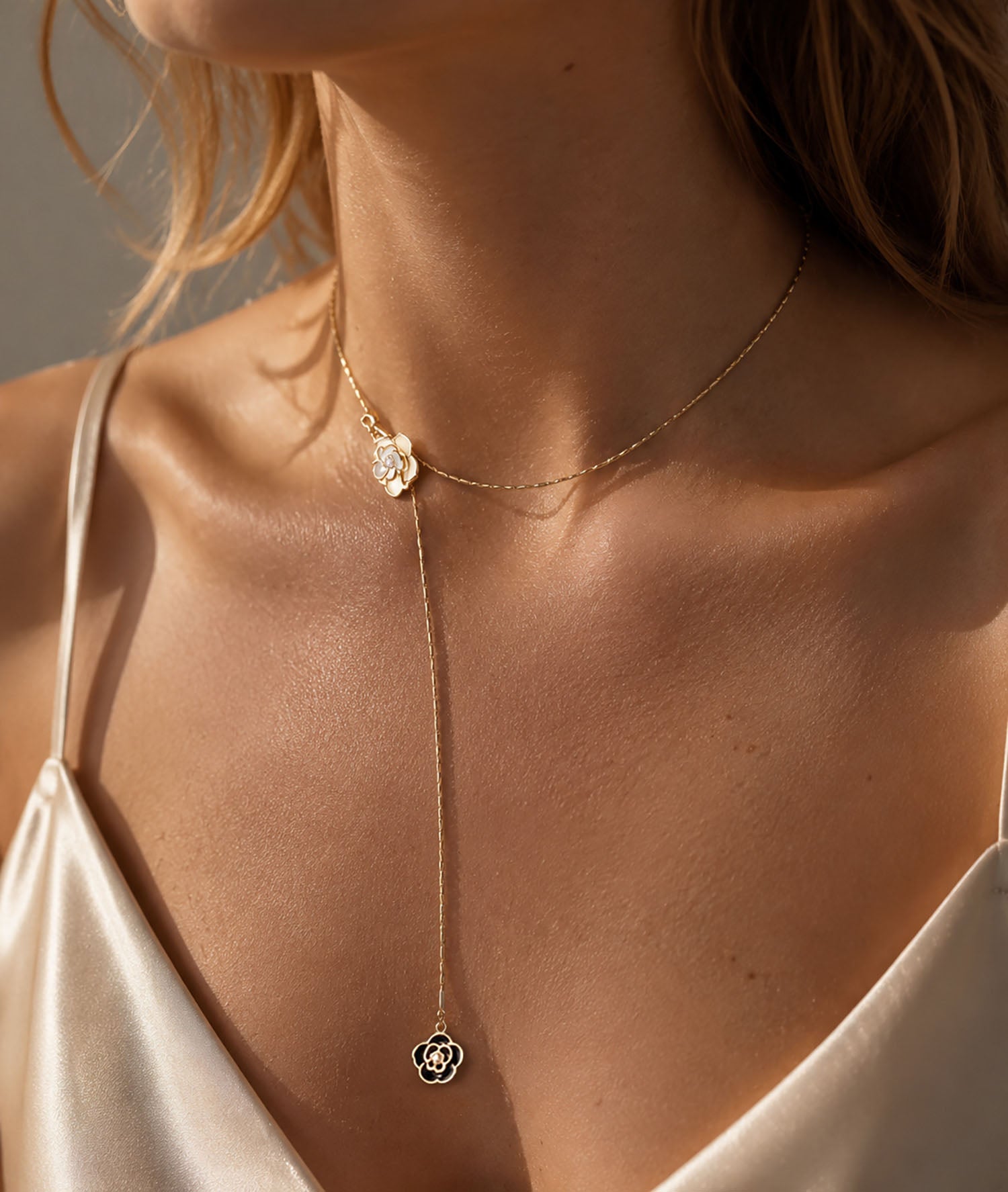 Elegant woman wearing a timeless gold-tone lariat necklace featuring black and white camellia flower pendants in warm sunlight.