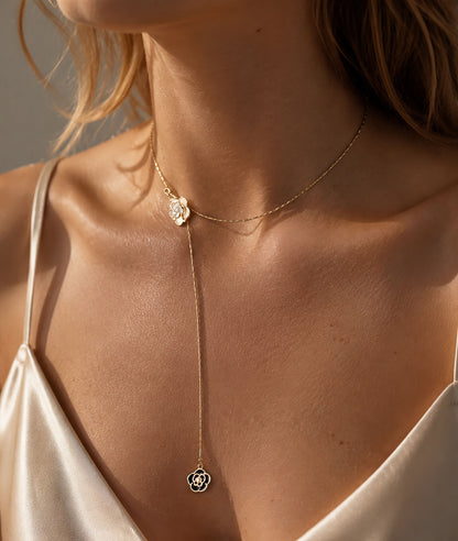 Elegant woman wearing a timeless gold-tone lariat necklace featuring black and white camellia flower pendants in warm sunlight.