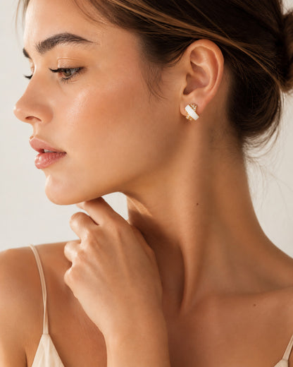 Elegant woman wearing delicate gold-tone criss-cross stud earrings with sparkling zirconia.