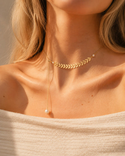 Beautiful woman wearing a Grecian-inspired 18K gold-tone wheat ear lariat necklace with a pearl drop in warm, natural sunlight.