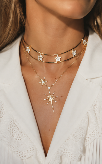 Beautiful woman wearing a crisp white shirt, styling a bold layered gold-tone necklace featuring a double-wire star choker and a long sunburst pendant.