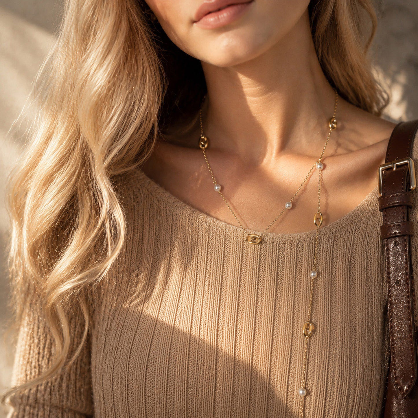 Woman wearing a versatile long gold-tone pearl and anchor chain necklace in warm sunlight.