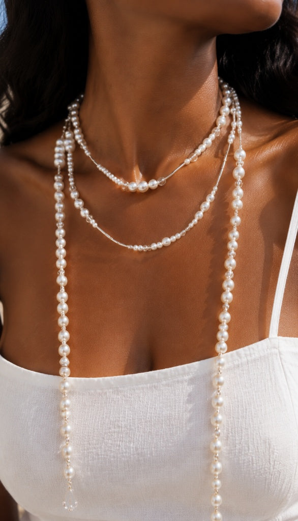 Beautiful sun-kissed woman wearing a white dress, styling an extra-long gold-tone scattered pearl necklace wrapped elegantly twice around her neck.