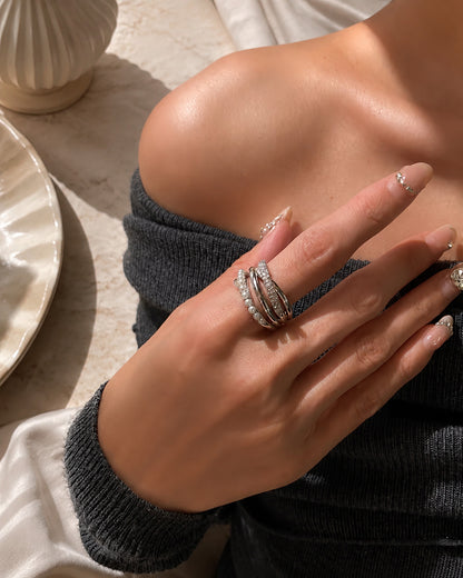 Close-up of a woman's hand styling a bold silver-tone multi-layer crossover ring featuring crystal pearls and zirconia accents in warm sunlight.