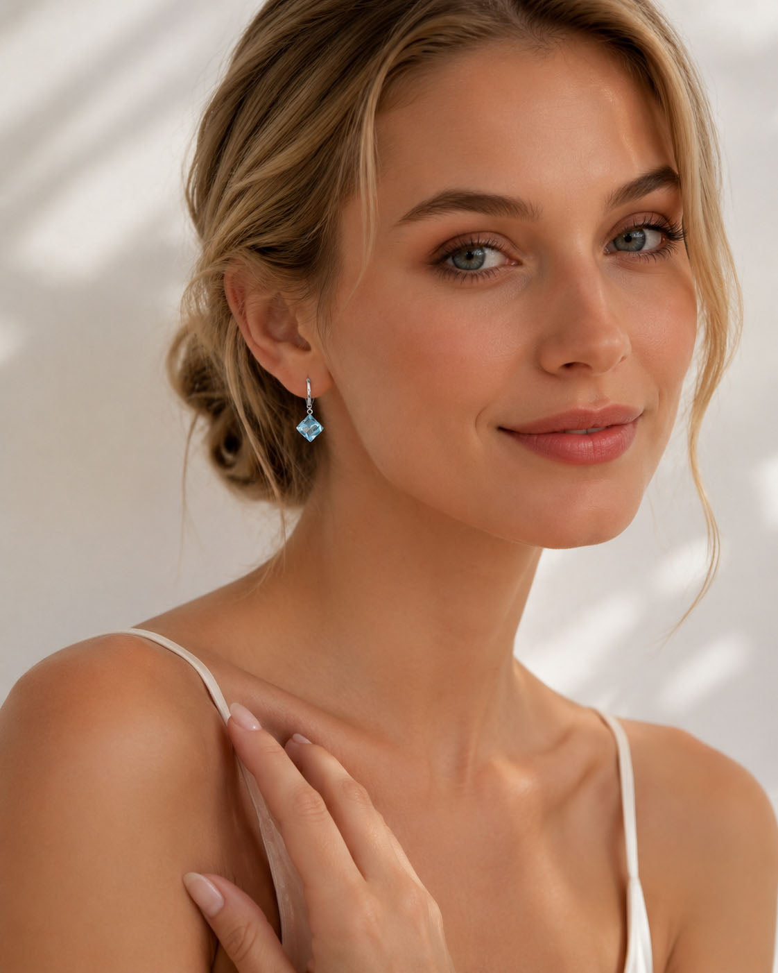 Elegant woman smiling, wearing radiant ocean blue square zirconia drop earrings in white gold-tone.