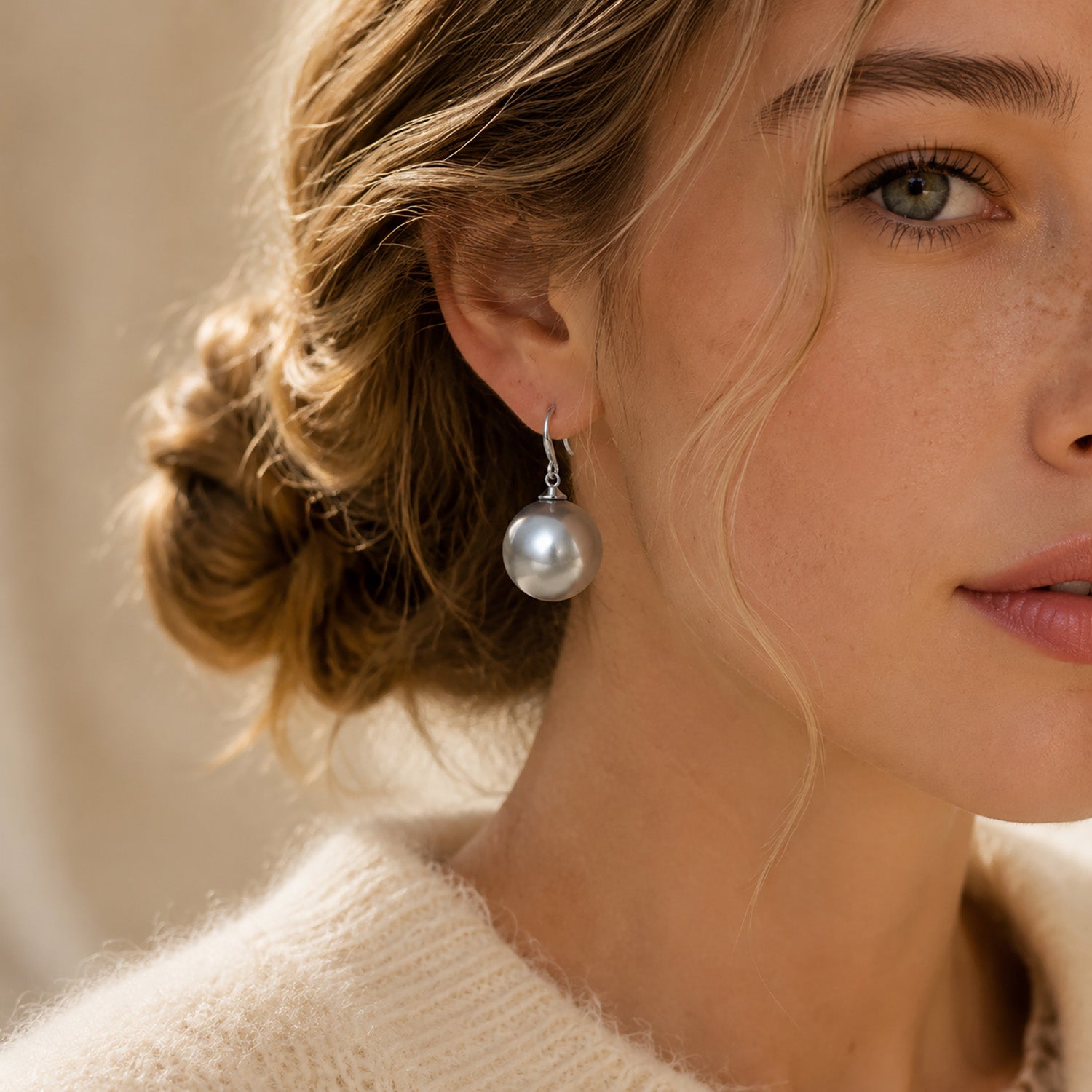 Beautiful woman wearing striking 19mm oversized silver-tone pearl drop earrings with a cozy knit sweater.