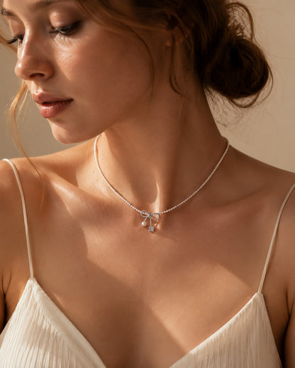 Elegant woman wearing a sweet pearl bowknot choker necklace in white gold-tone.