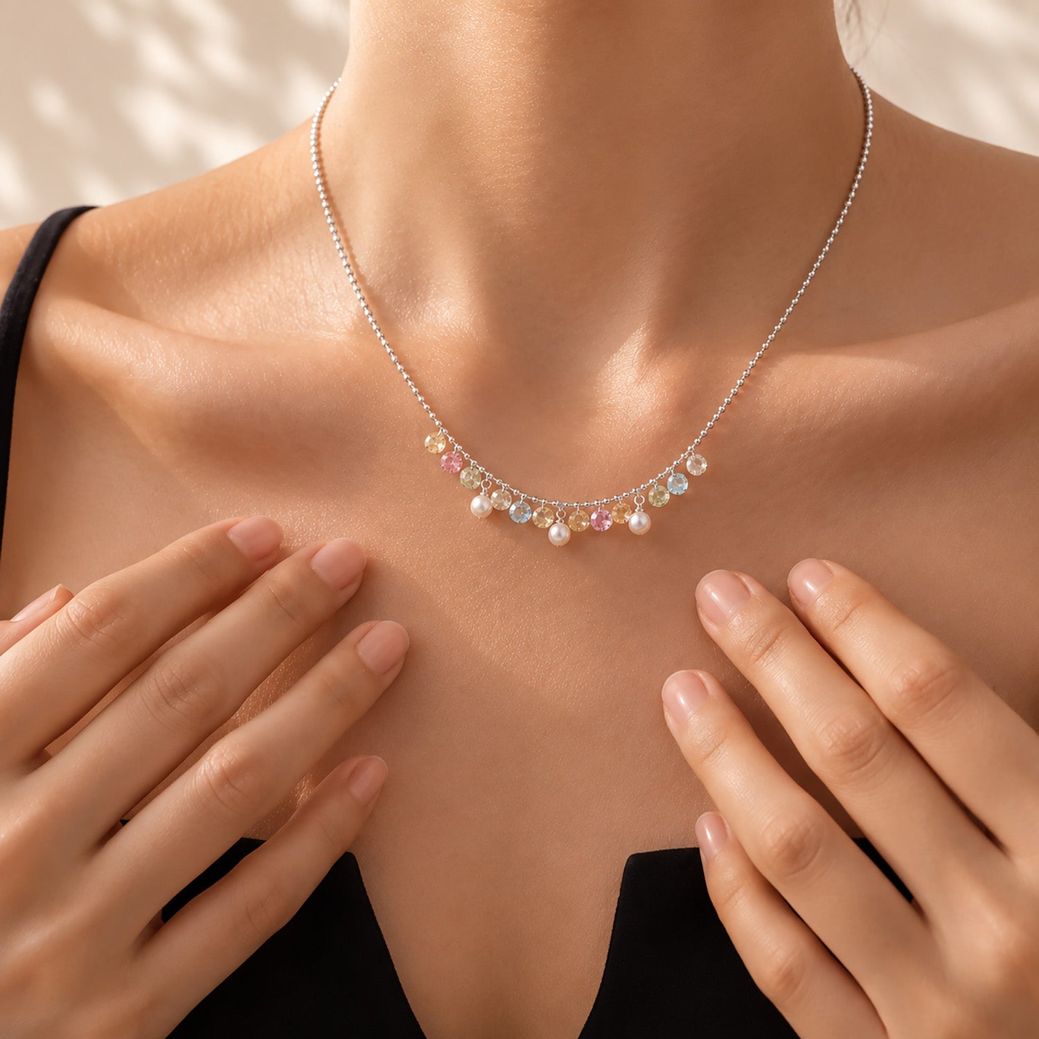 Close up of a woman's collarbone wearing a vibrant rainbow zirconia and pearl fringe necklace in white gold-tone.